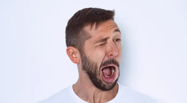 Hombre con barba y tics nerviosos musculares, guiñando un ojo y con la boca abierta en un gesto de sorpresa o grito.