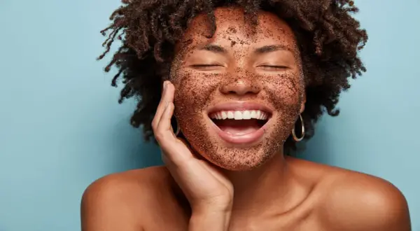 Mujer sonríe feliz con mascarilla exfoliante en el rostro. Descubre cómo exfoliar la piel para una tez radiante.