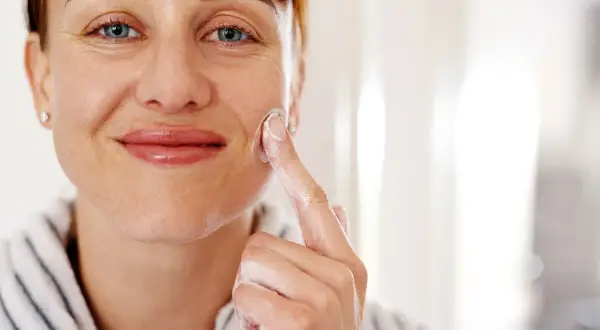 Mujer sonriente aplicándose crema con glicerina para la cara. Su piel luce hidratada y cuidada.