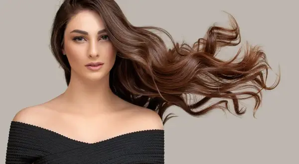 Mujer con cabello castaño ondulado y largo, con un vestido negro. ¿Buscas cómo quitar tinte?