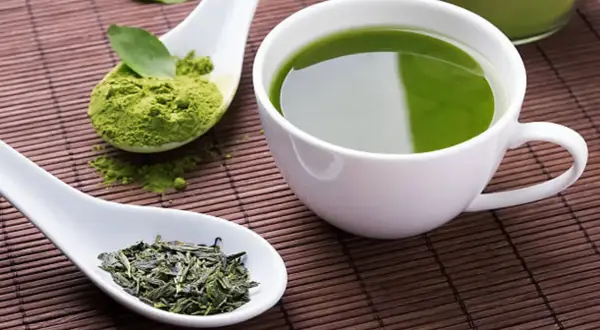 Té verde en polvo y hojas secas junto a una taza de té verde. Descubre cuál es el mejor té para adelgazar.