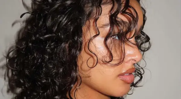 Primer plano de una mujer con una hermosa forma de pelo rizado y oscuro, con mechones cayendo sobre su rostro.