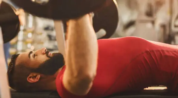 Hombre con barba haciendo press de banca. Si buscas qué hacer para engordar, el entrenamiento de fuerza es clave.