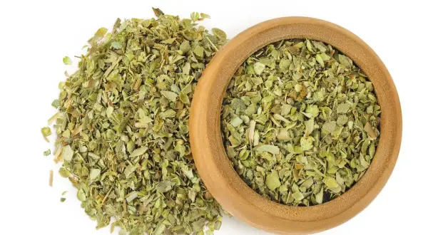Hierbas secas de mejorana en un cuenco de madera y esparcidas. Descubre las mejorana propiedades para tu cocina y bienestar.