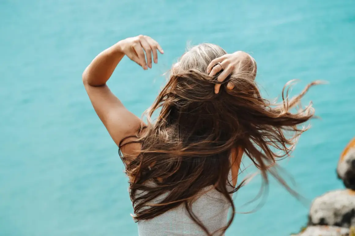 Mujer con cabello largo y castaño, jugando con su pelo. Una forma natural de como disimular las canas es con peinados que aporten volumen.