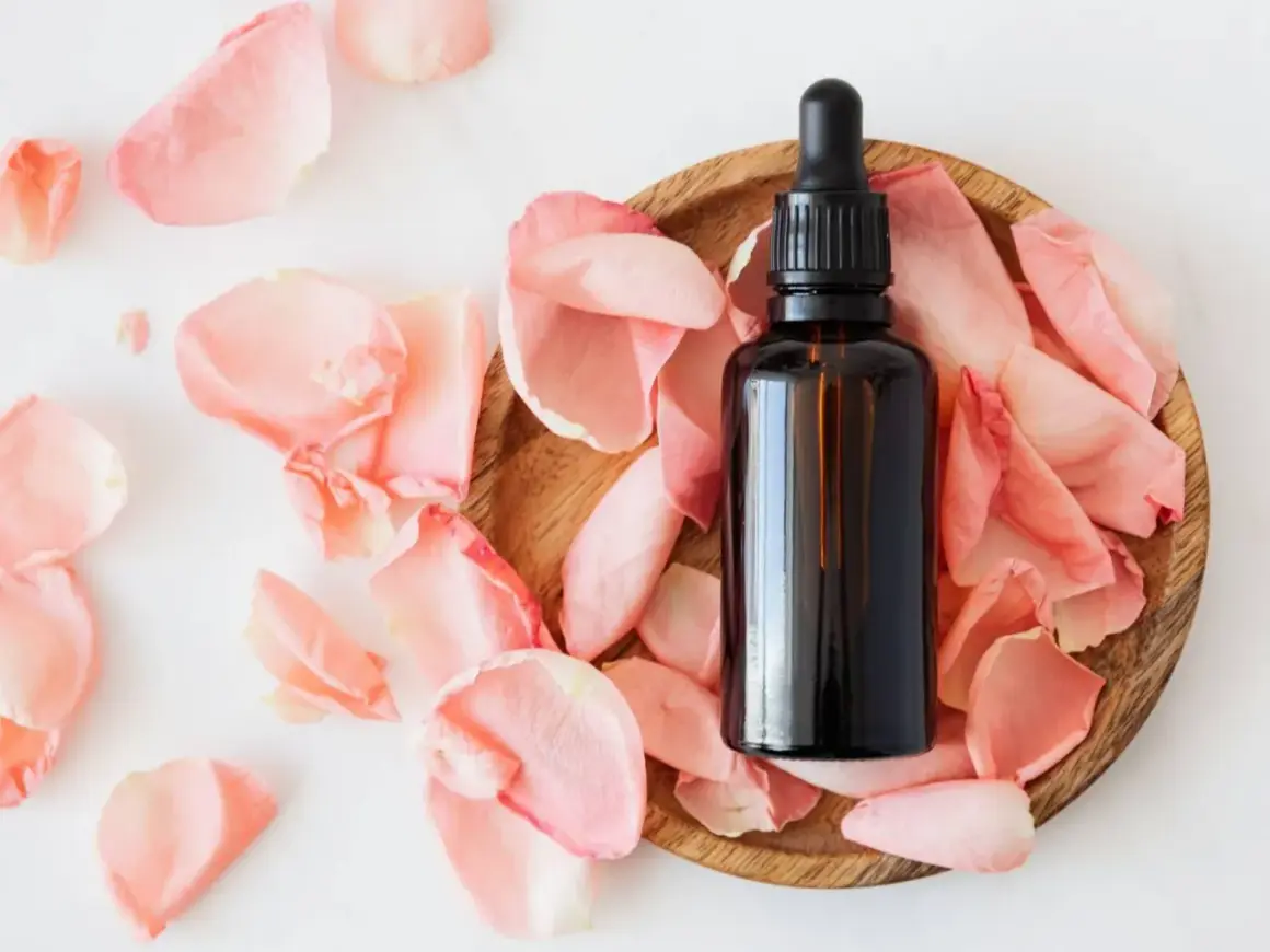 Frasco de aceites esenciales despigmentantes rodeado de pétalos de rosa.