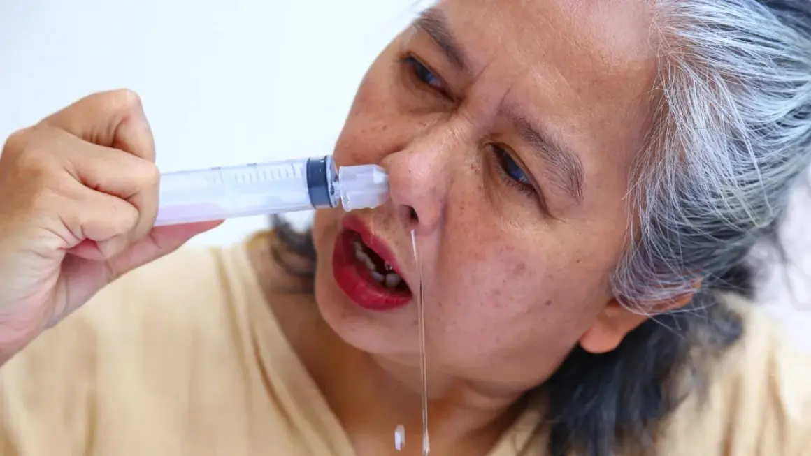 Mujer mayor se aplica suero fisiológico casero con jeringa para aliviar congestión nasal.
