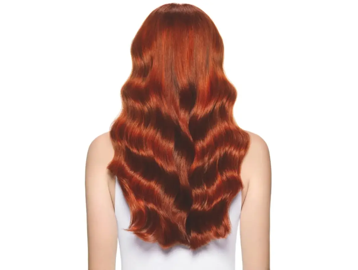 Cabello largo y ondulado con un vibrante color de pelo cobrizo dorado que brilla bajo la luz.