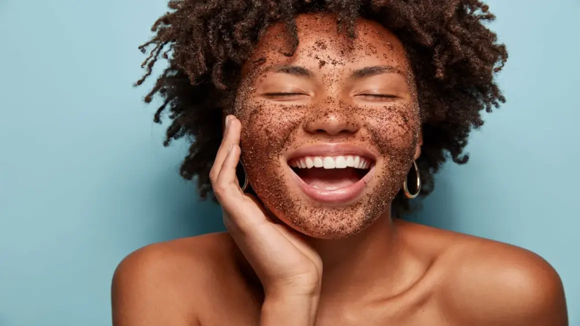 Mujer sonríe feliz con mascarilla exfoliante en el rostro. Descubre cómo exfoliar la piel para una tez radiante.