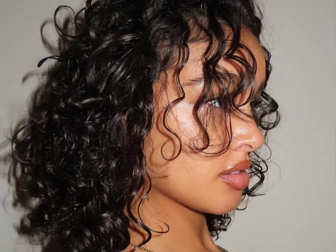 Primer plano de una mujer con una hermosa forma de pelo rizado y oscuro, con mechones cayendo sobre su rostro.