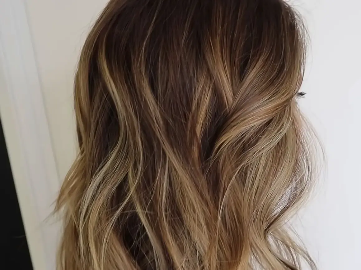 Cabello ondulado con un degradado de rubio a raíz castaña, con reflejos dorados que le dan luz.