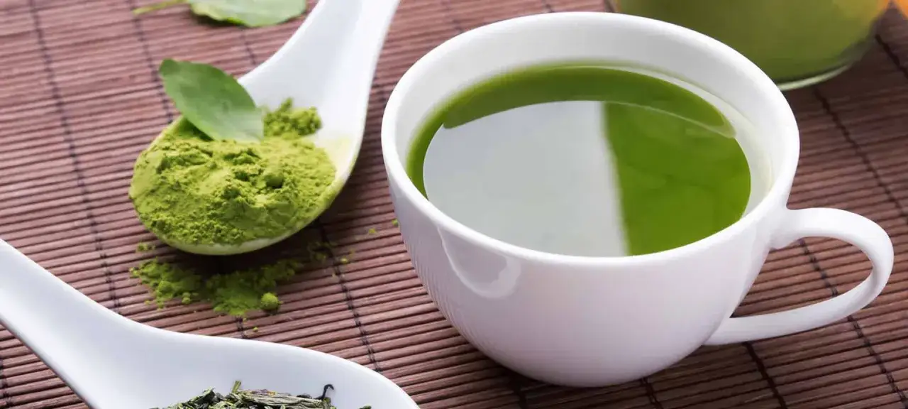 T&eacute; verde vibrante en taza blanca, polvo de matcha en cuchara, ideal para la cara y el bienestar.