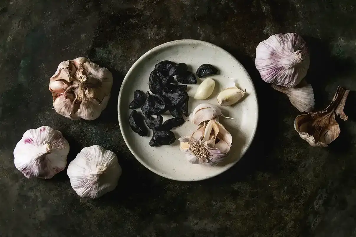 Ajo negro y fresco en plato, mostrando los beneficios del ajo negro para la salud.