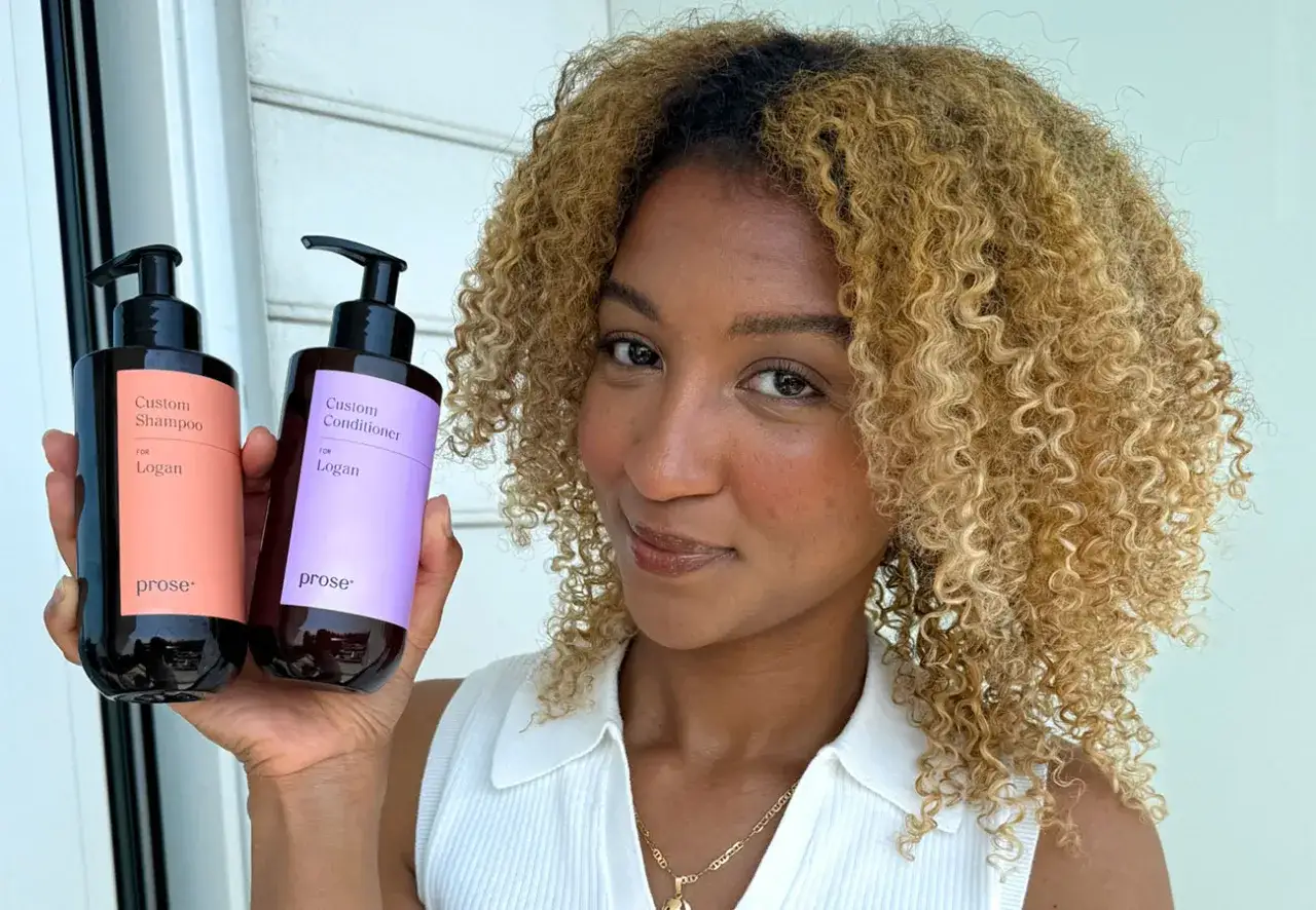 Mujer con cabello rizado y rubio muestra dos botellas de champú y acondicionador personalizados, ideales para quienes buscan como aclarar el pelo.
