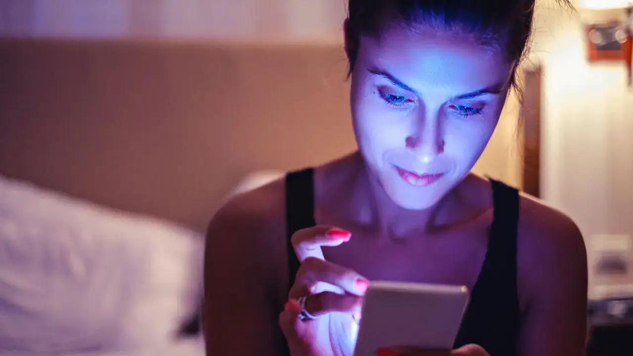 Mujer absorta en su m&oacute;vil, iluminada por la luz azul. &iquest;Qu&eacute; es la luz azul? Es la que emiten las pantallas, afectando nuestro sue&ntilde;o.
