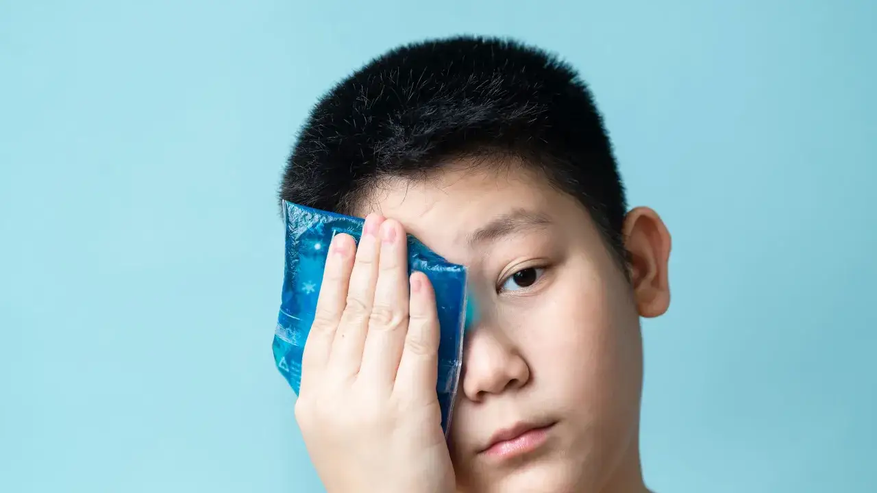 Niño aplica compresa fría en el ojo, buscando alivio con remedios caseros para la conjuntivitis.