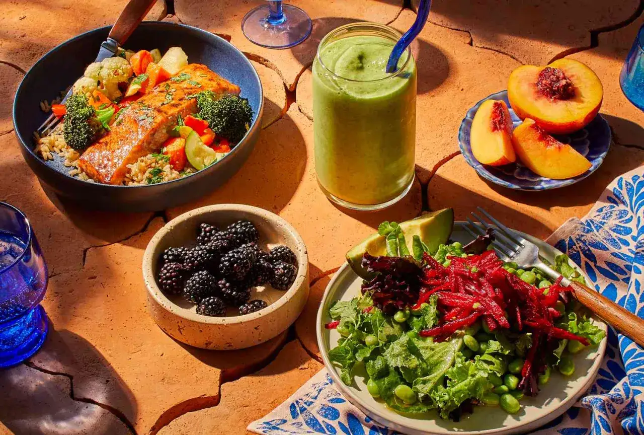 Un plato de salm&oacute;n con arroz y verduras, una ensalada vibrante, moras y duraznos son ejemplos de carbohidratos y otros alimentos saludables.