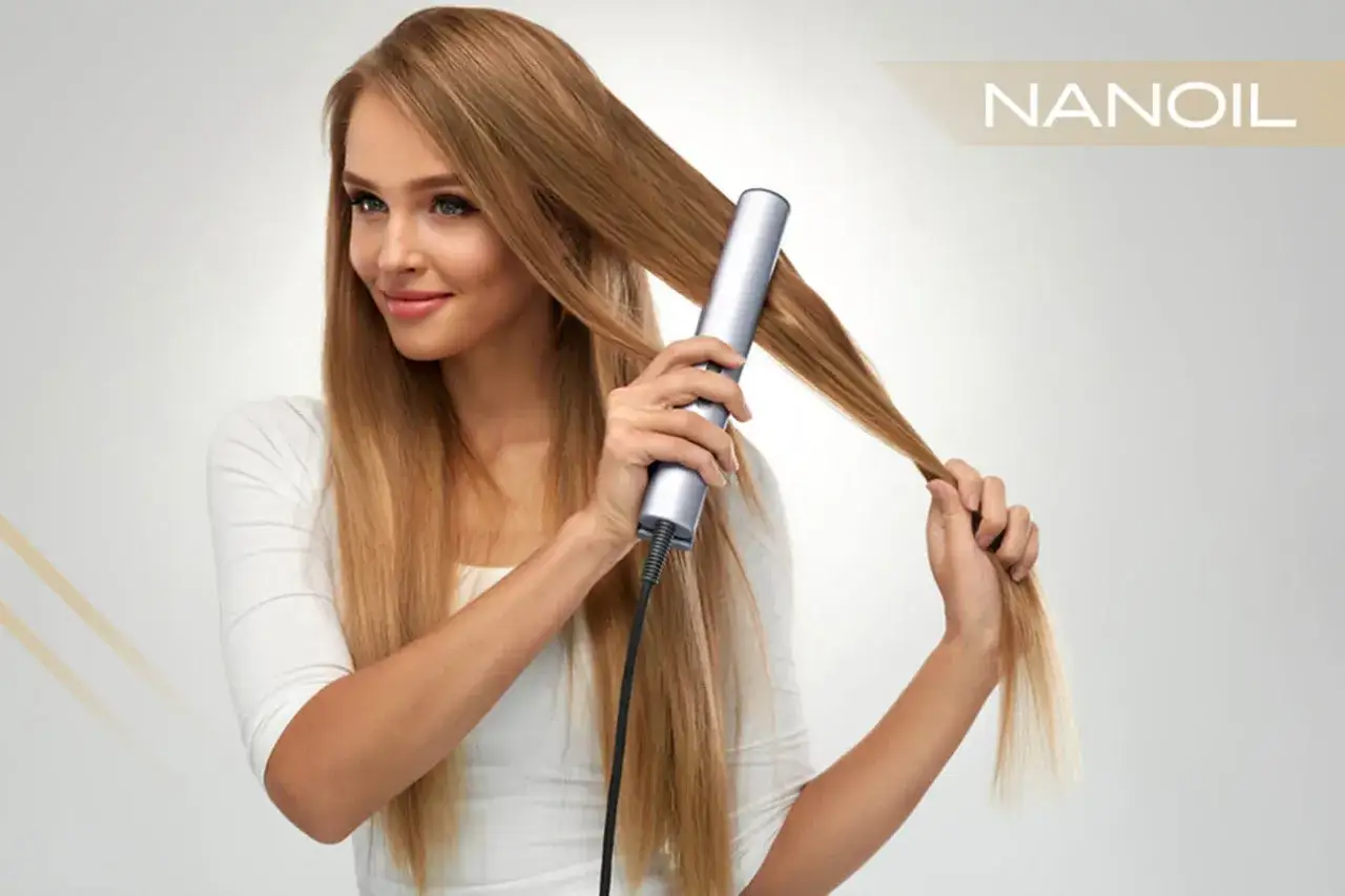 Mujer sonriente usa una plancha para alisar el pelo rubio y largo. El resultado es un cabello liso y sedoso.