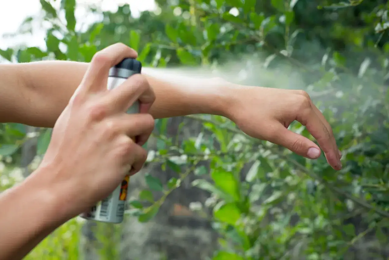 Persona aplica aceite repelente de mosquitos en su brazo para protegerse de picaduras mientras disfruta del aire libre.