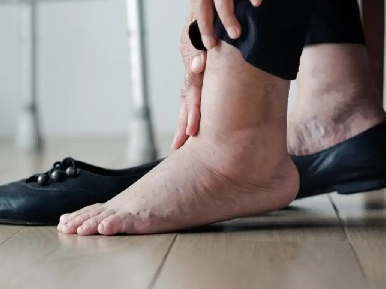Persona mayor se toca los tobillos hinchados, con un zapato negro al lado.