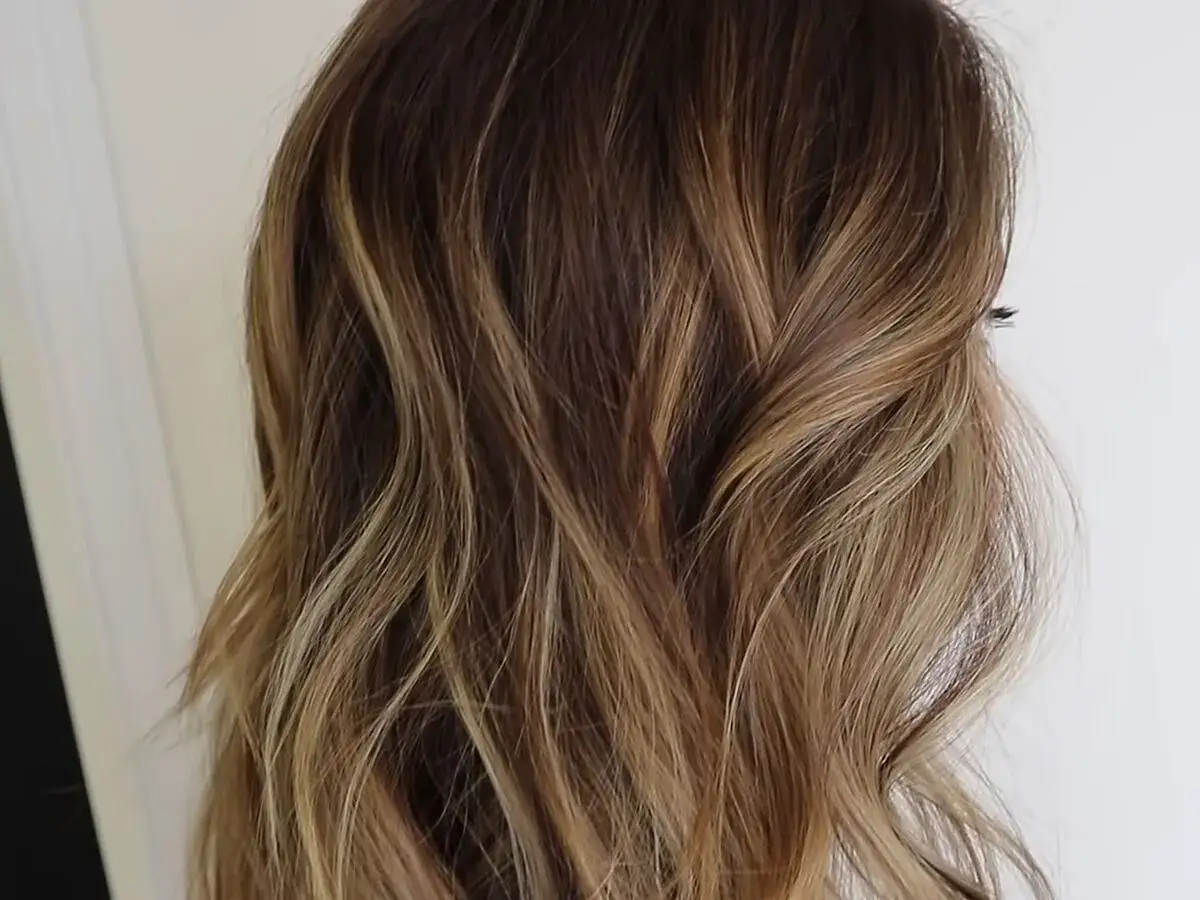Cabello ondulado con un degradado de rubio a raíz castaña, creando un efecto natural y luminoso.