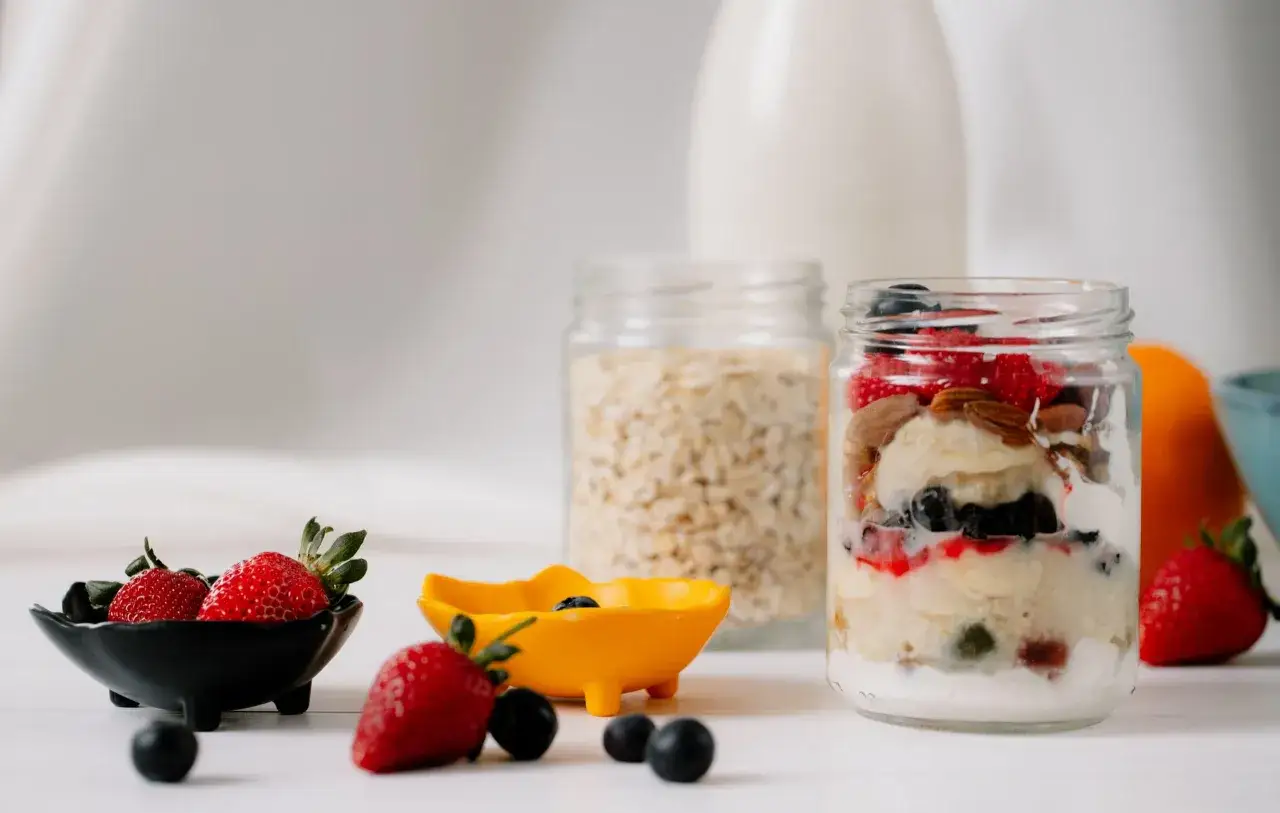 Un frasco con capas de yogur, avena, frutas y frutos secos, ideal para una merienda sana. Fresas y ar&aacute;ndanos acompa&ntilde;an.