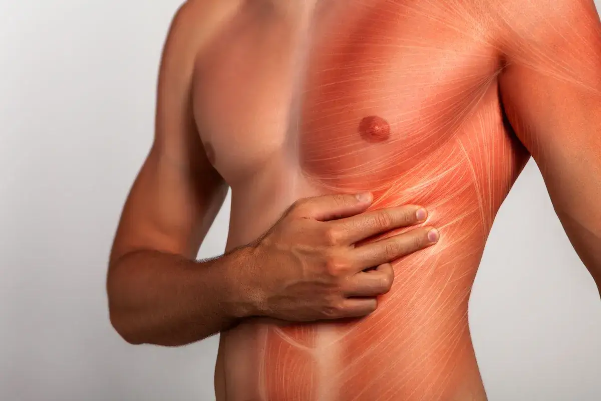 Hombre con la mano en el costado derecho, sintiendo pinchazos debajo de las costillas. La piel muestra un enrojecimiento y líneas que simulan dolor muscular.