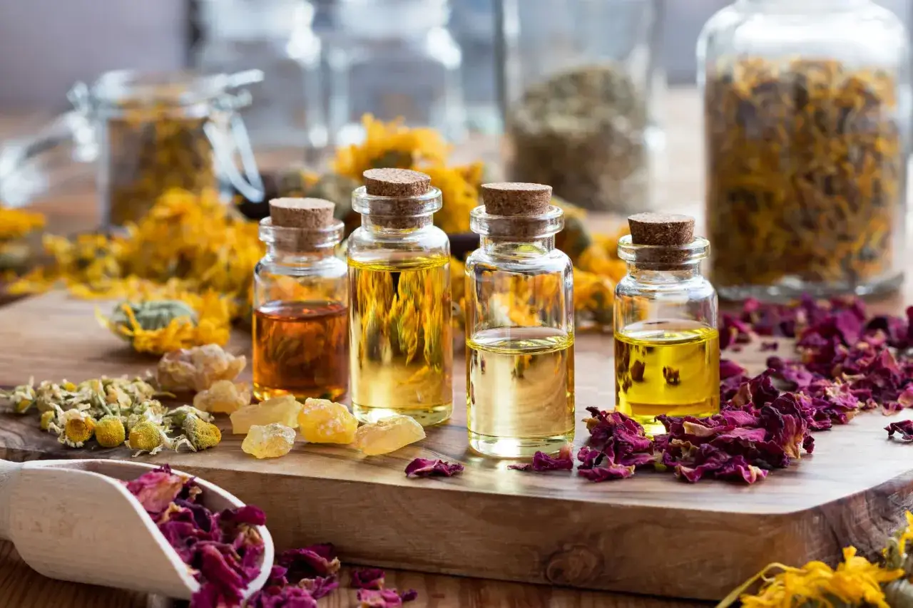 Botellas con aceites esenciales y pétalos de rosa, flores secas y resina. La imagen evoca sinergias de aceites esenciales para el bienestar.