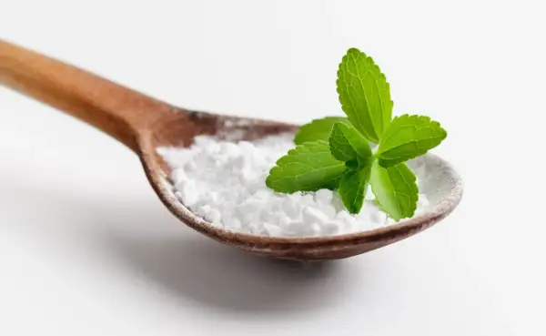 Cucharada de polvo blanco, que es la stevia, con hojas verdes frescas encima.