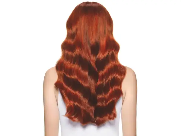 Cabello largo y ondulado con un vibrante color de pelo cobrizo dorado que brilla bajo la luz.