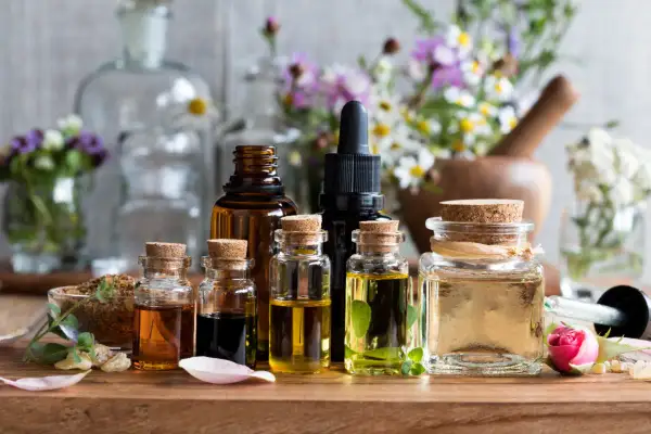 Frascos de vidrio con aceites esenciales para aromaterapia, rodeados de flores y hierbas.