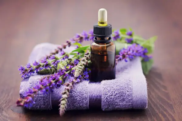 Frasco de aceite esencial de salvia con flores moradas sobre toalla. Descubre las maravillosas aceite de salvia propiedades para tu bienestar.