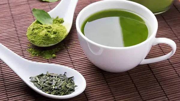 Té verde en polvo y hojas secas junto a una taza de té verde. Descubre cuál es el mejor té para adelgazar.