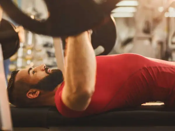 Hombre con barba haciendo press de banca. Si buscas qué hacer para engordar, el entrenamiento de fuerza es clave.
